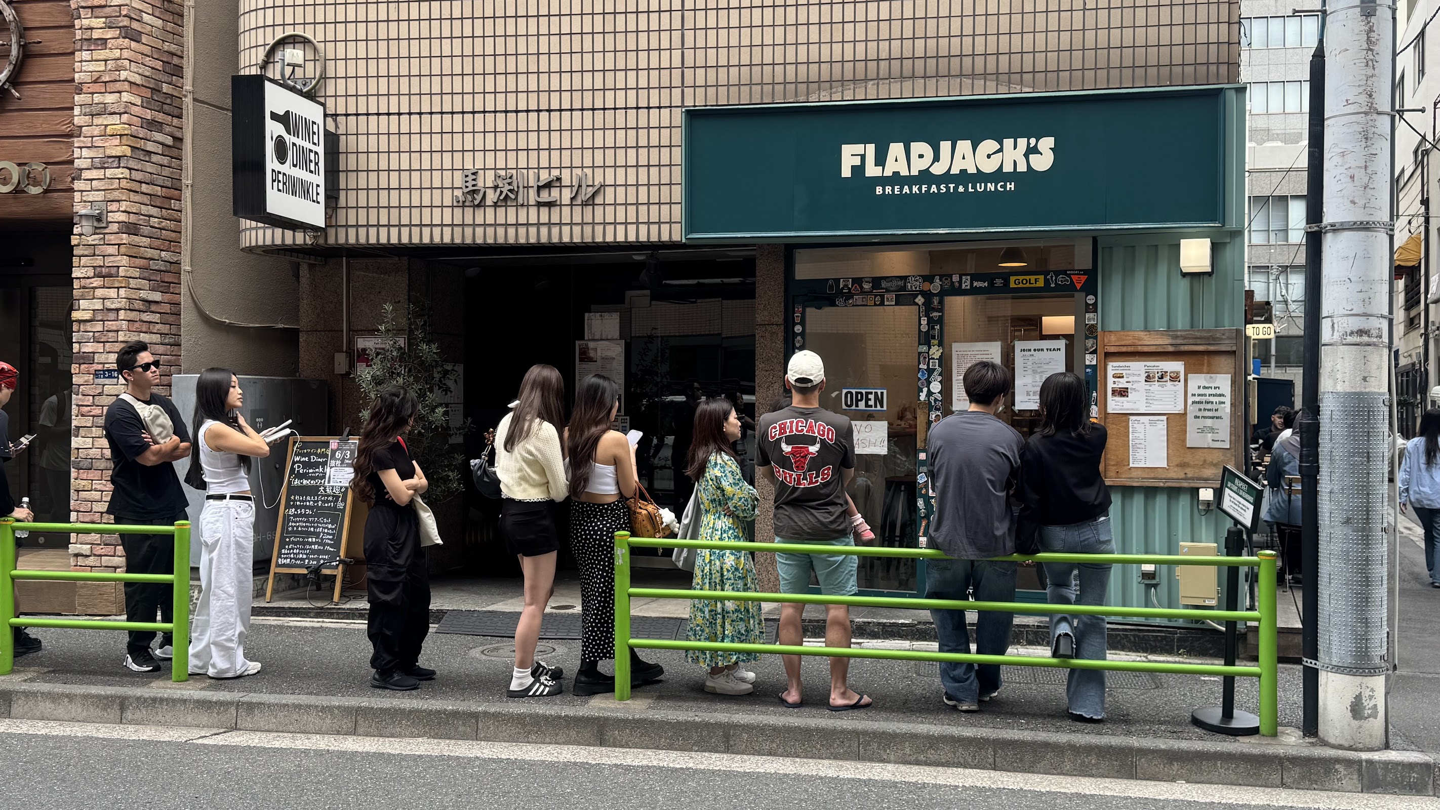 緑の鉄柵沿いに10人ほどが列を作り、ミントグリーン波板外壁のFLAPJACK'S店頭前で開店を待つ昼間の外観