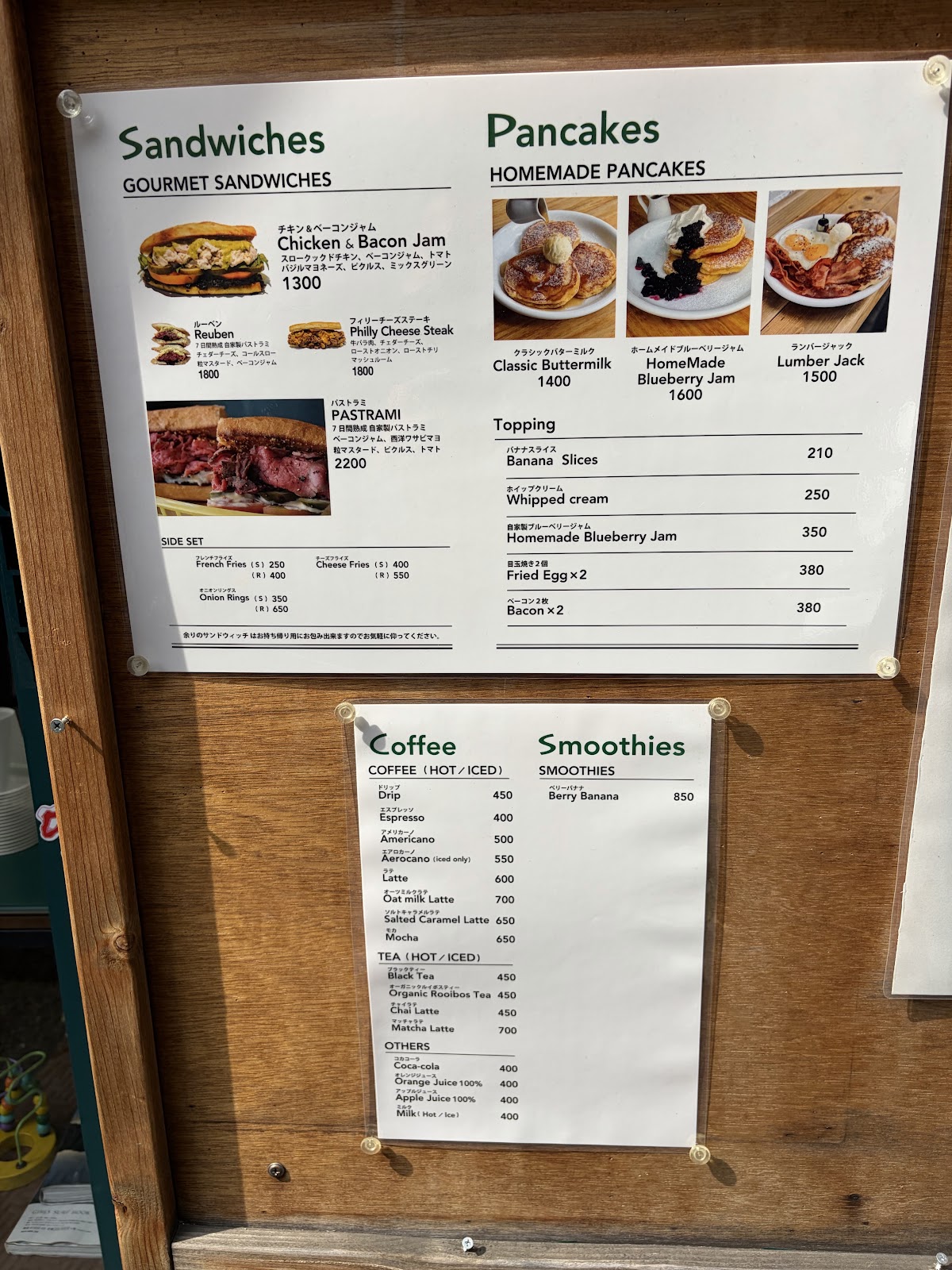 木製パネルに貼られたサンドイッチ・パンケーキ・コーヒー・スムージーの価格表。Philly Cheese Steak ¥1,800、Classic Buttermilk ¥1,400などが読み取れる